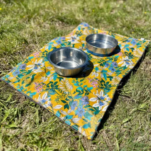 Tapis pour gamelles de chiens en tissu imperméable aux motifs floraux et fond moutarde.