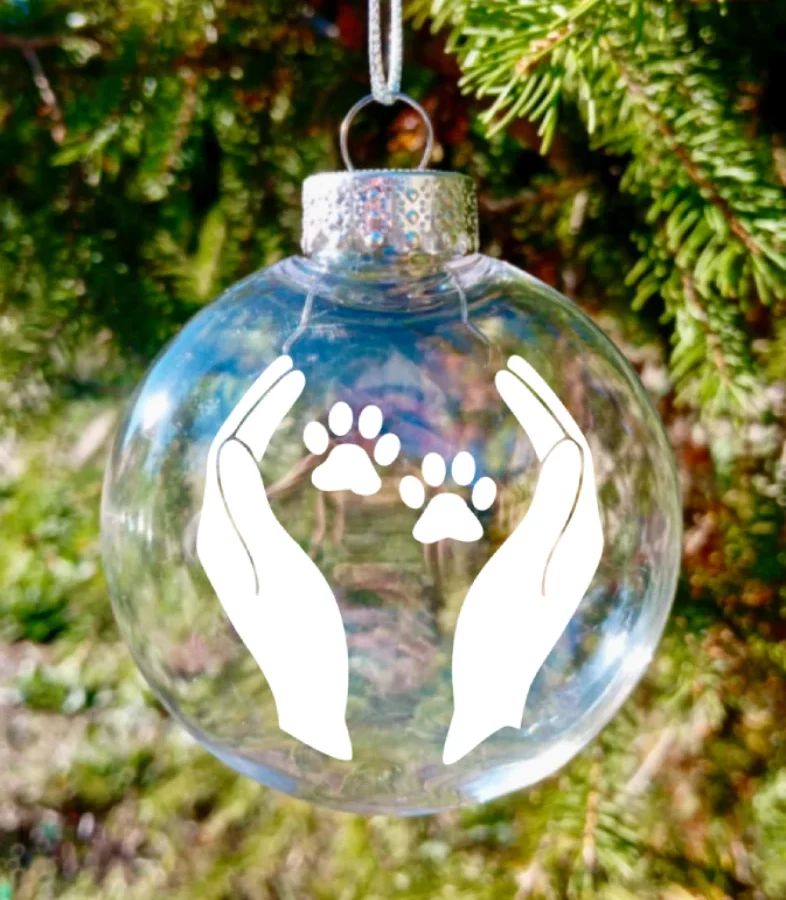 Boule de Noël avec motif blanc de pattes de chien dans des mains. Possibilité de personnaliser. Artisanat français.